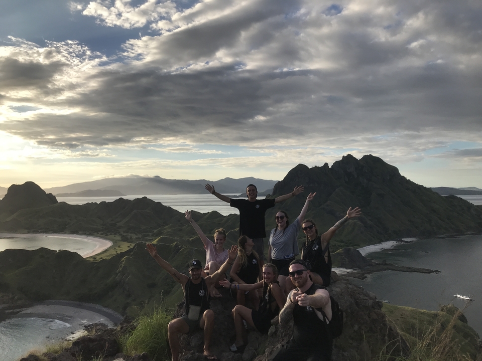Groupe de personnes sur une colline avec vue panoramique sur une baie et des montagnes.