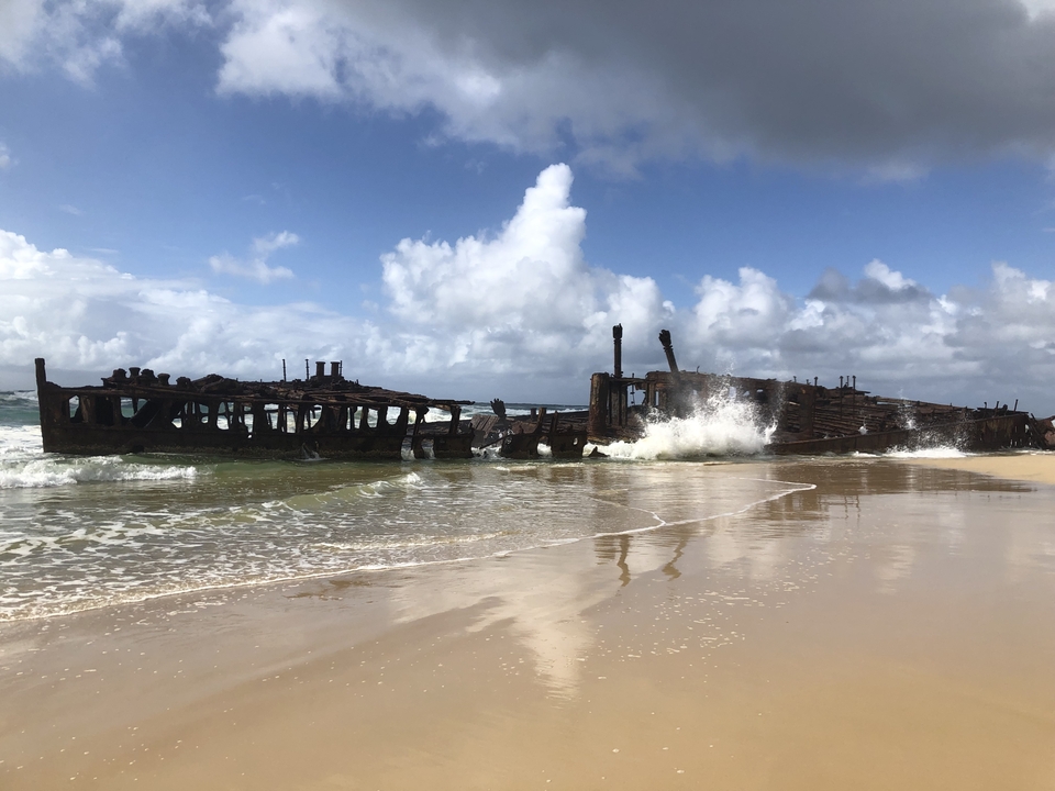 Wreck of a ship on a sandy beach with waves splashing against it.
