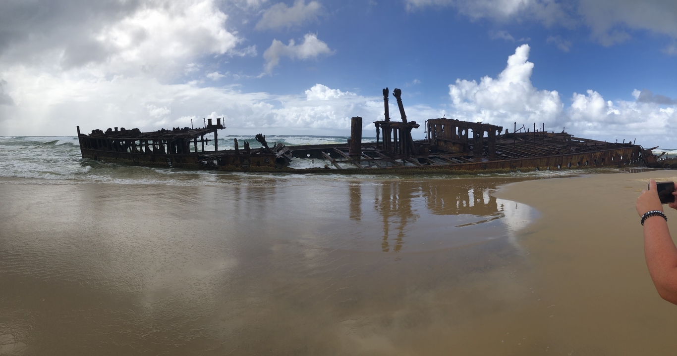 Wreck of a ship on a sandy beach with waves splashing against it.