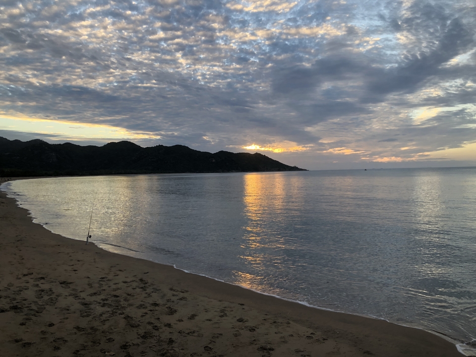 Sunset over a calm beach with silhouetted hills.