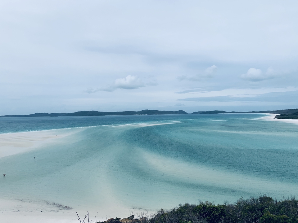 White sand beach with turquoise waters and distant hills.