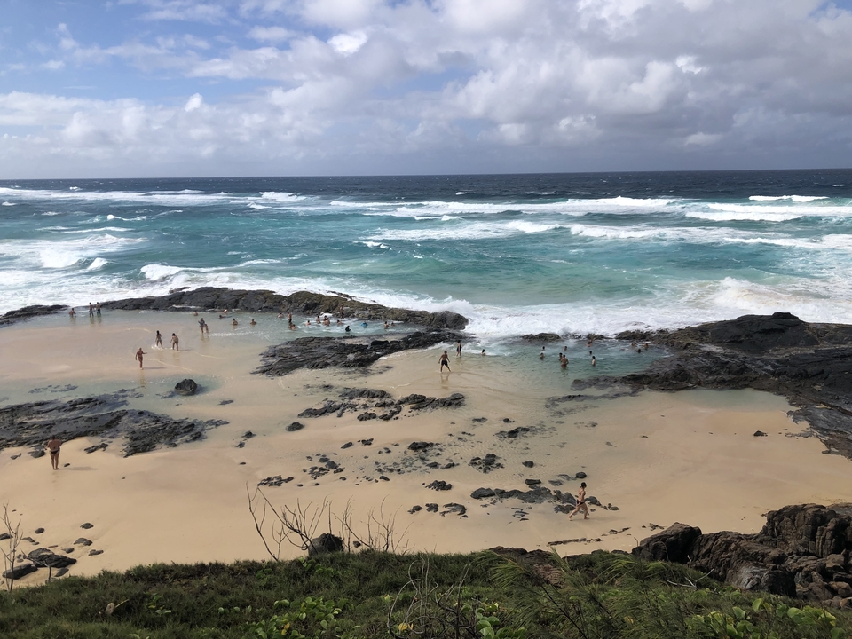 Natural tidal pools with people swimming in them along a rocky beach.