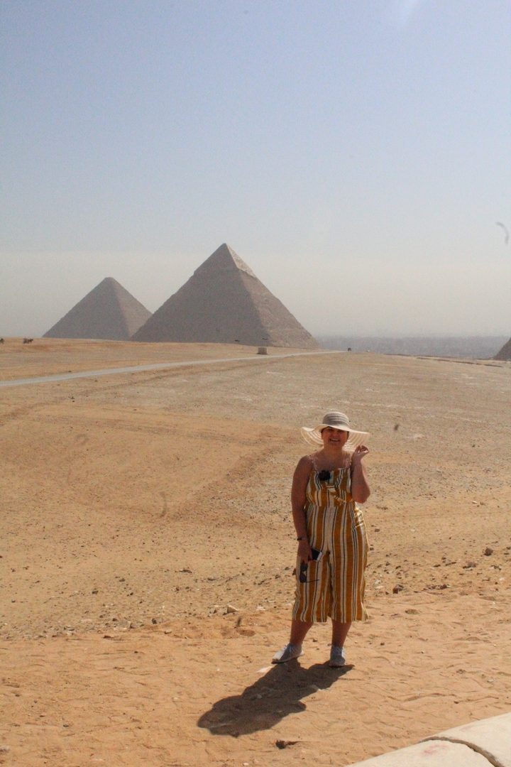 Person standing near pyramids with desert landscape.