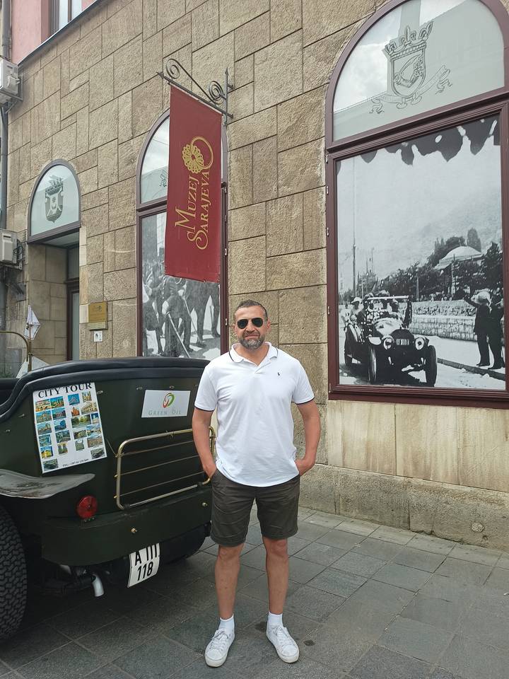 A man standing beside a vintage car on a street.
