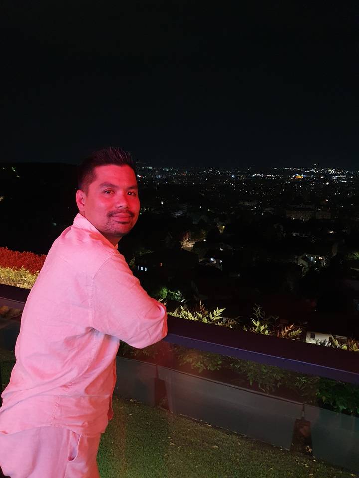 A person posing with city lights in the background at night.