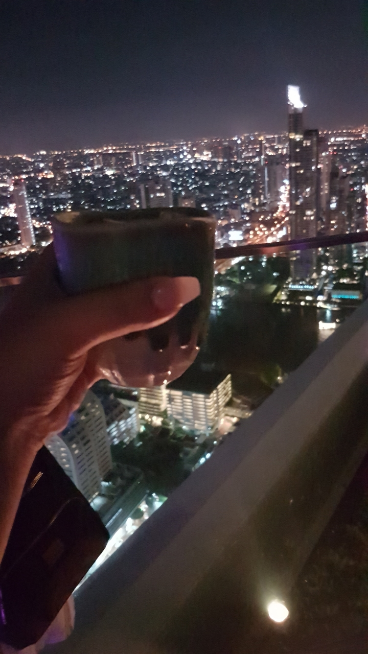 Main tenant une boisson avec vue sur l'horizon urbain la nuit.