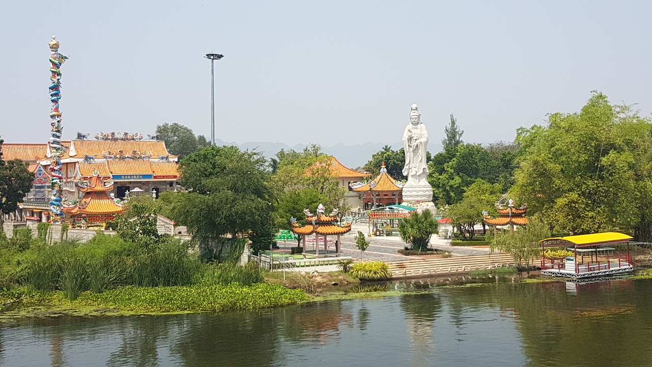 Complexe de temples coloré avec une grande statue au bord de la rivière.