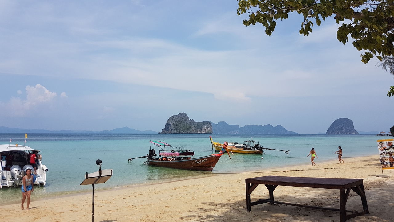 Des bateaux amarrés près d'une plage de sable avec des îles rocheuses au loin.