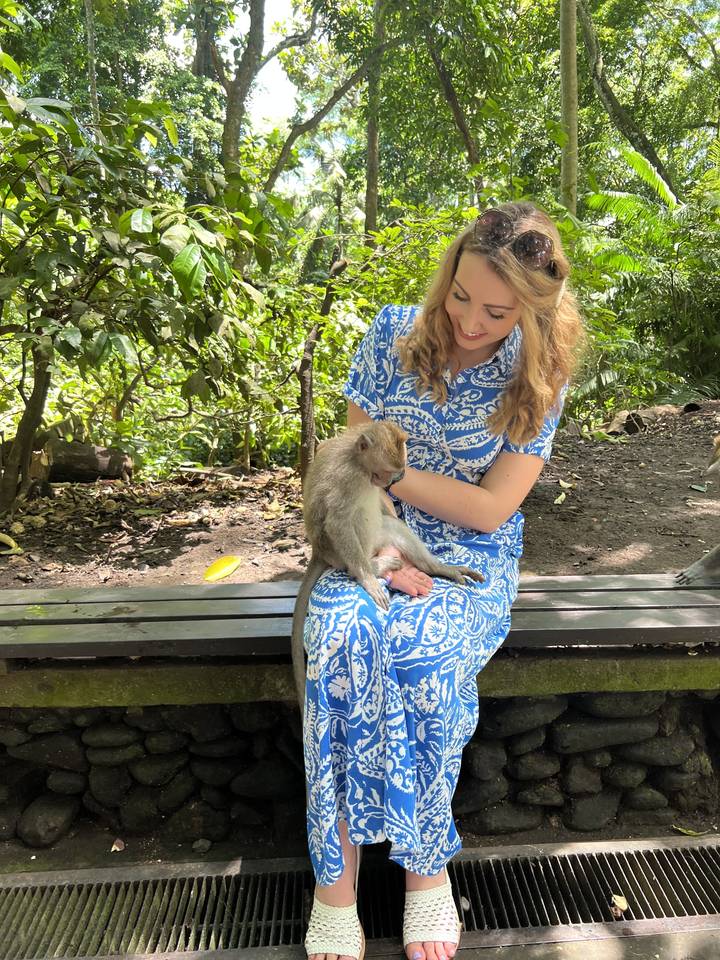 A person sitting with a monkey in a lush park.