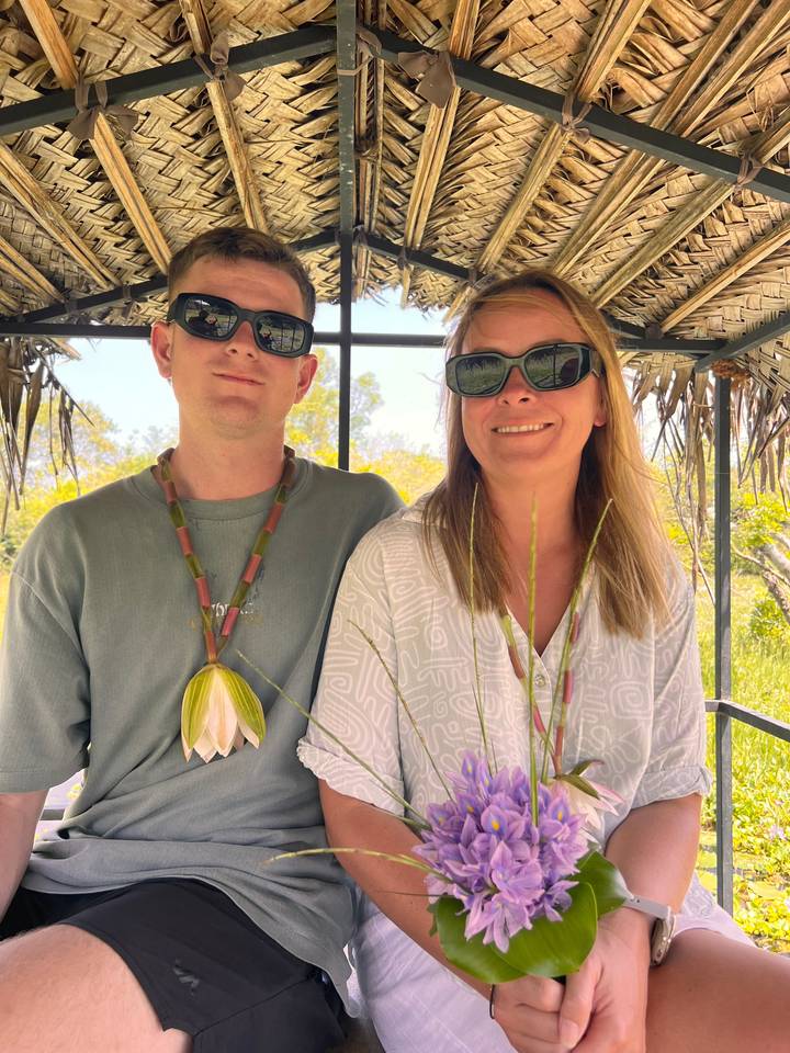 Deux personnes souriantes tenant des fleurs à l'intérieur d'une hutte.