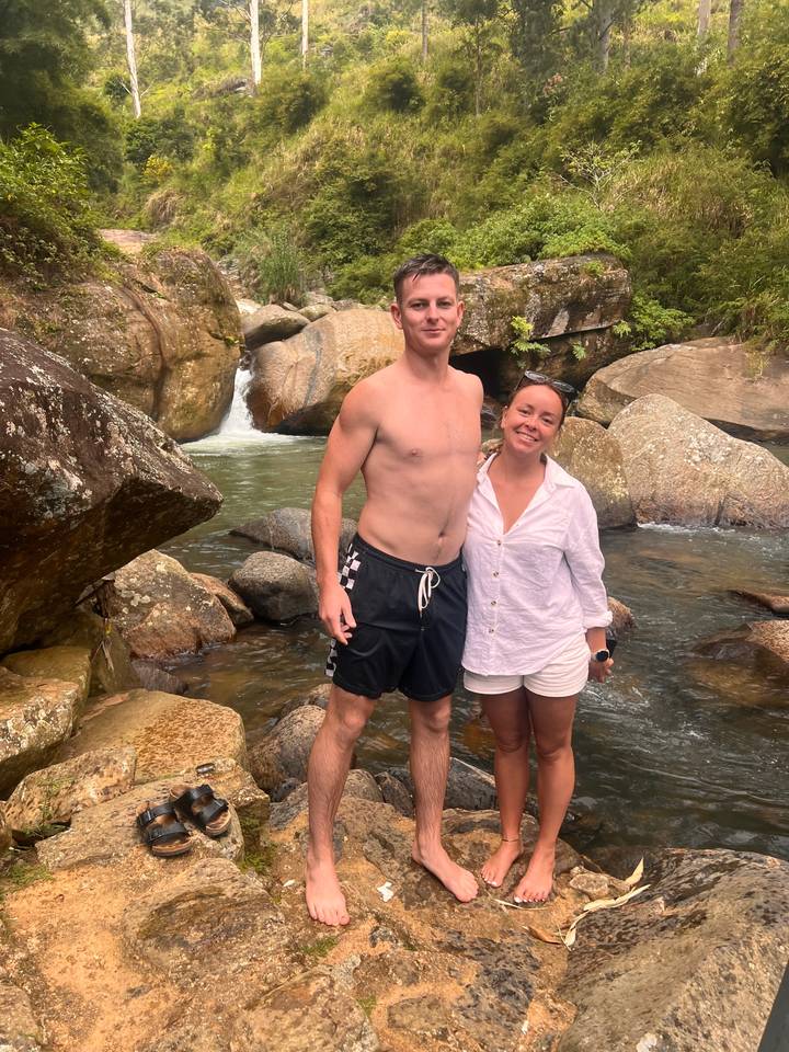 Deux personnes debout sur des rochers au bord d'un cours d'eau.