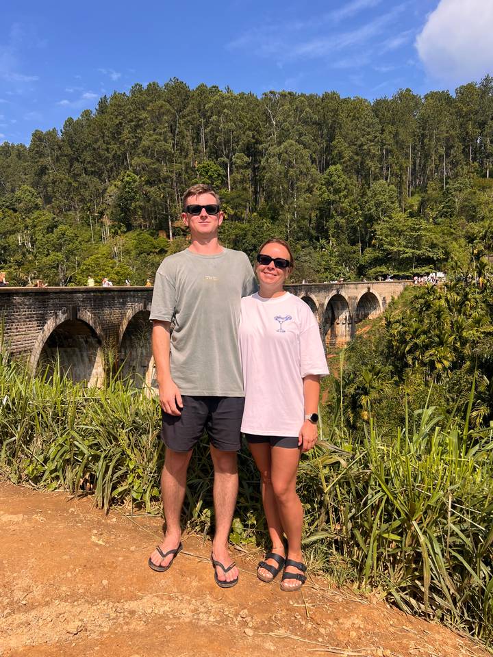 Deux personnes posant près d'un pont ferroviaire pittoresque avec une forêt verdoyante luxuriante.