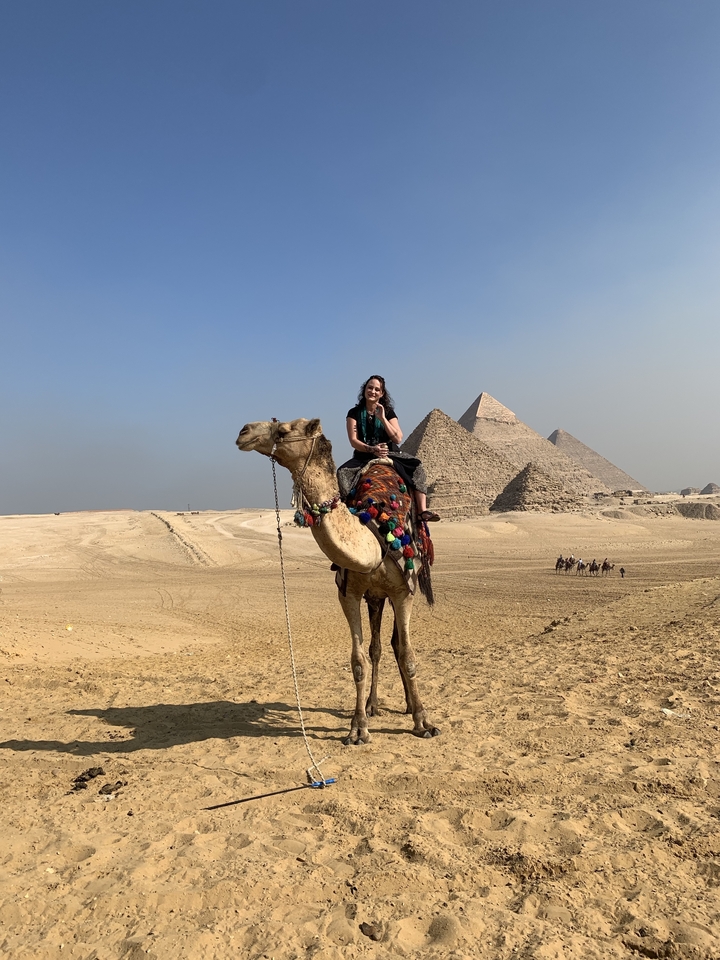Person riding a camel in front of the pyramids.