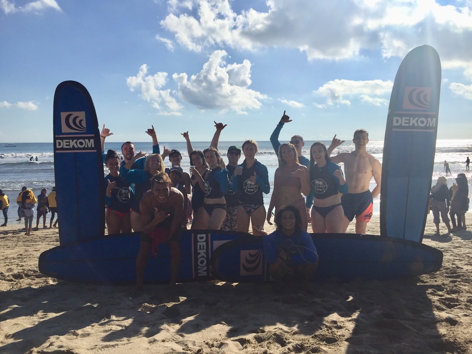 Group posing with surfboards on a sunny beach.