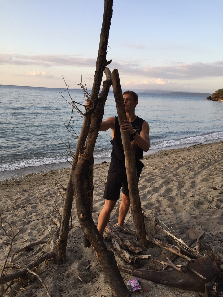 Personne construisant une structure avec du bois flotté sur une plage.