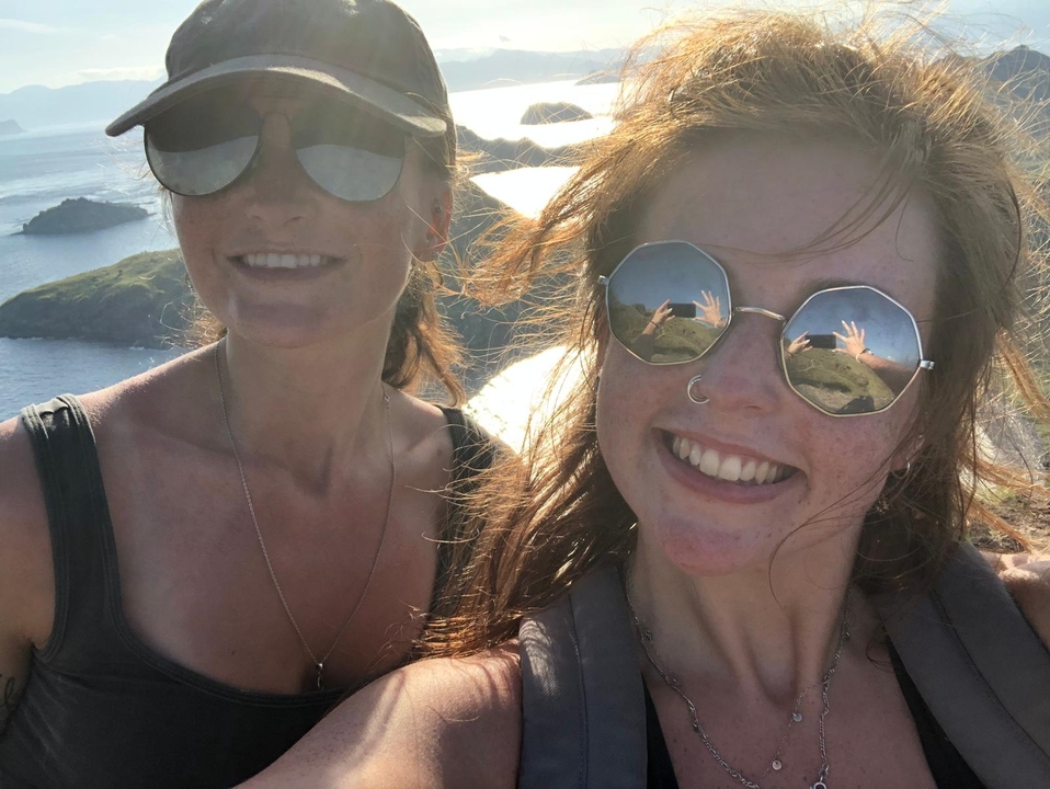 Deux personnes souriantes par une journée ensoleillée avec un paysage pittoresque en arrière-plan.