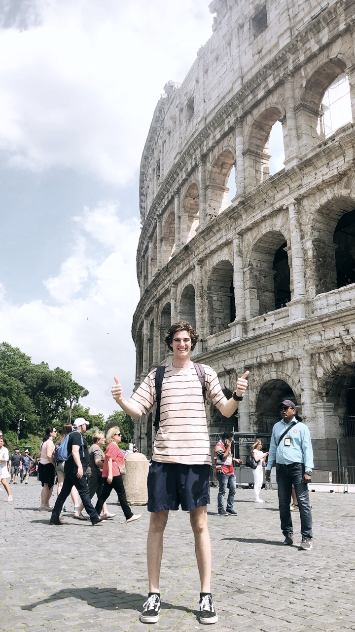 Person posing with thumbs up in front of the Colosseum.