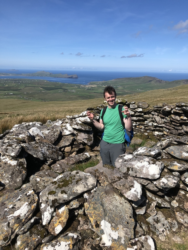 Person posing with stone ruins and distant landscape.