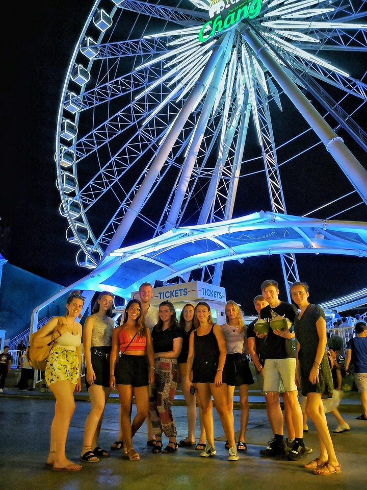 Group posing at night in front of a large illuminated Ferris wheel