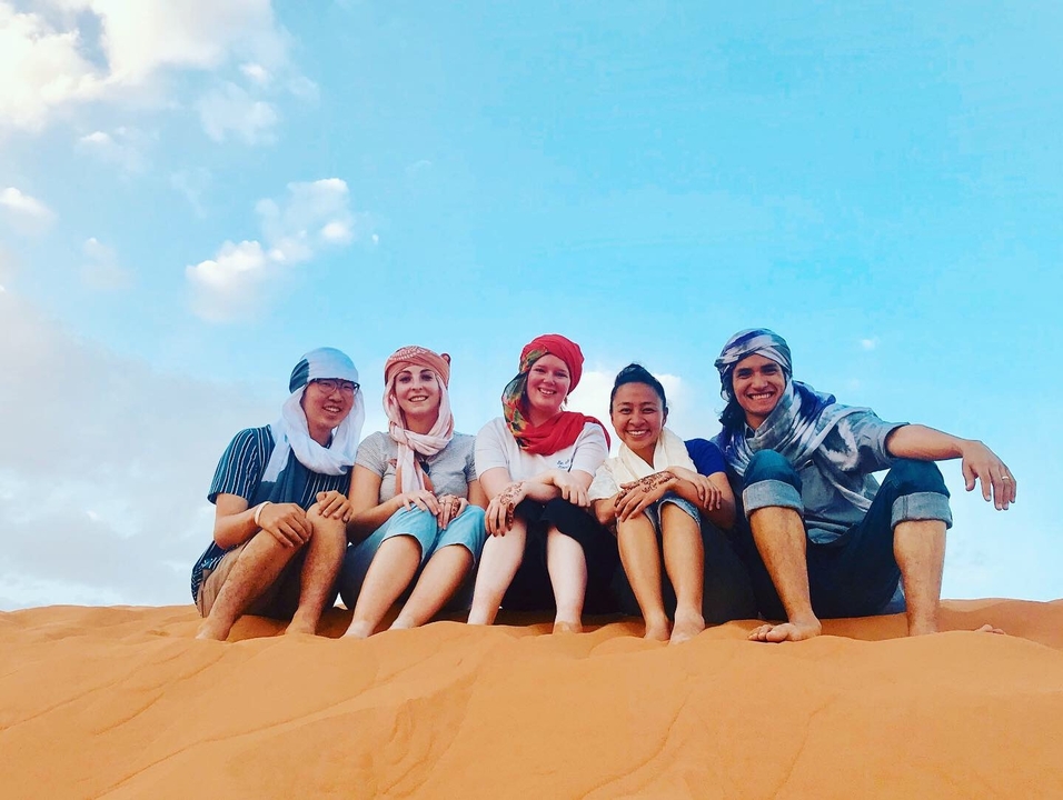 People sitting on sand dunes wearing traditional headscarves
