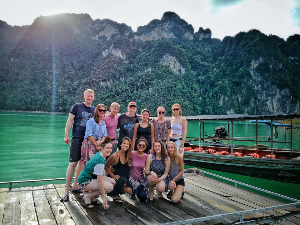 Group of people posing by a turquoise lake with mountains in the background.