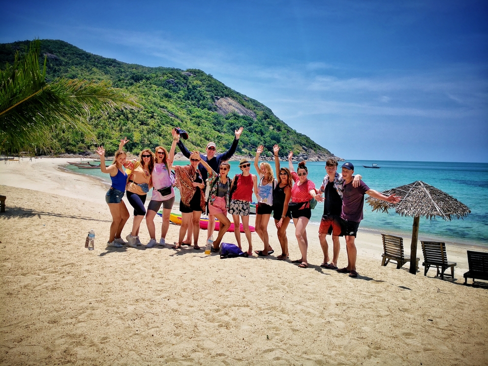 Group of people on a sunny beach with clear blue sky and water.