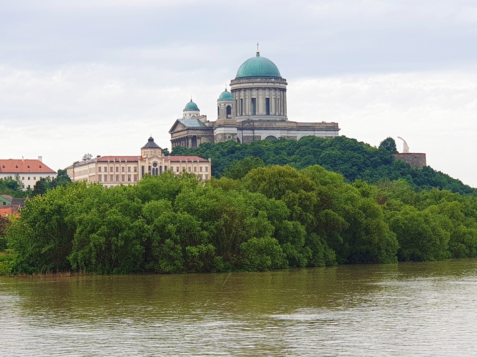 Une vue au bord de la rivière d'un grand bâtiment avec un dôme vert et des arbres.