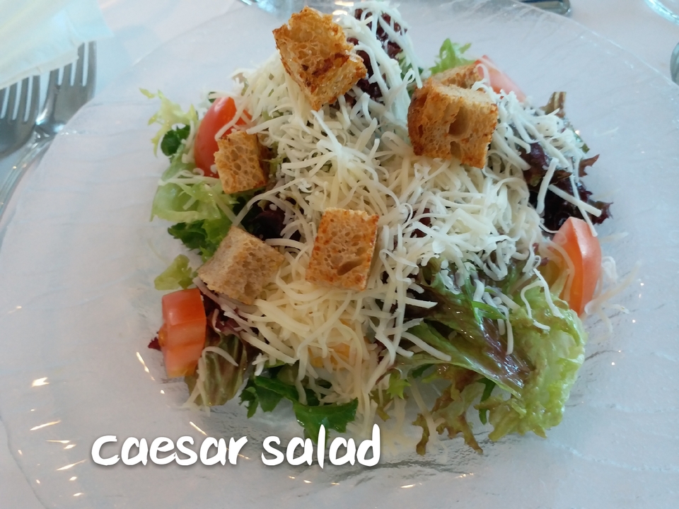 Une salade avec du fromage râpé, des croûtons, et des légumes verts à feuilles dans une assiette.