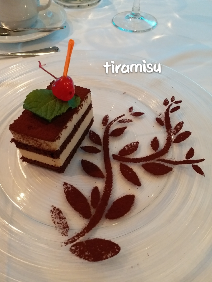 Un dessert avec un gâteau en couches et de la poudre de cacao sur une assiette décorée.