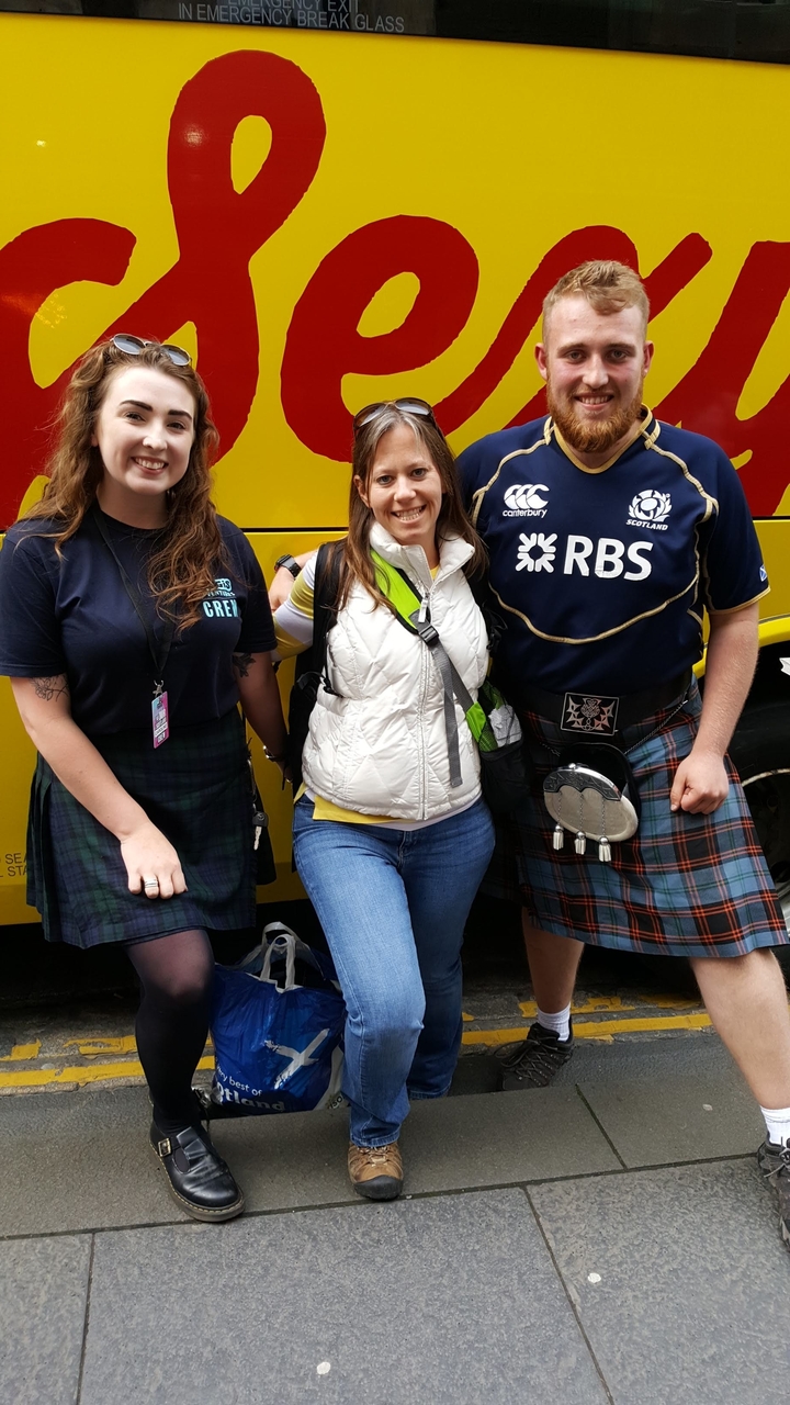 Three people in Scottish attire smiling outdoors.