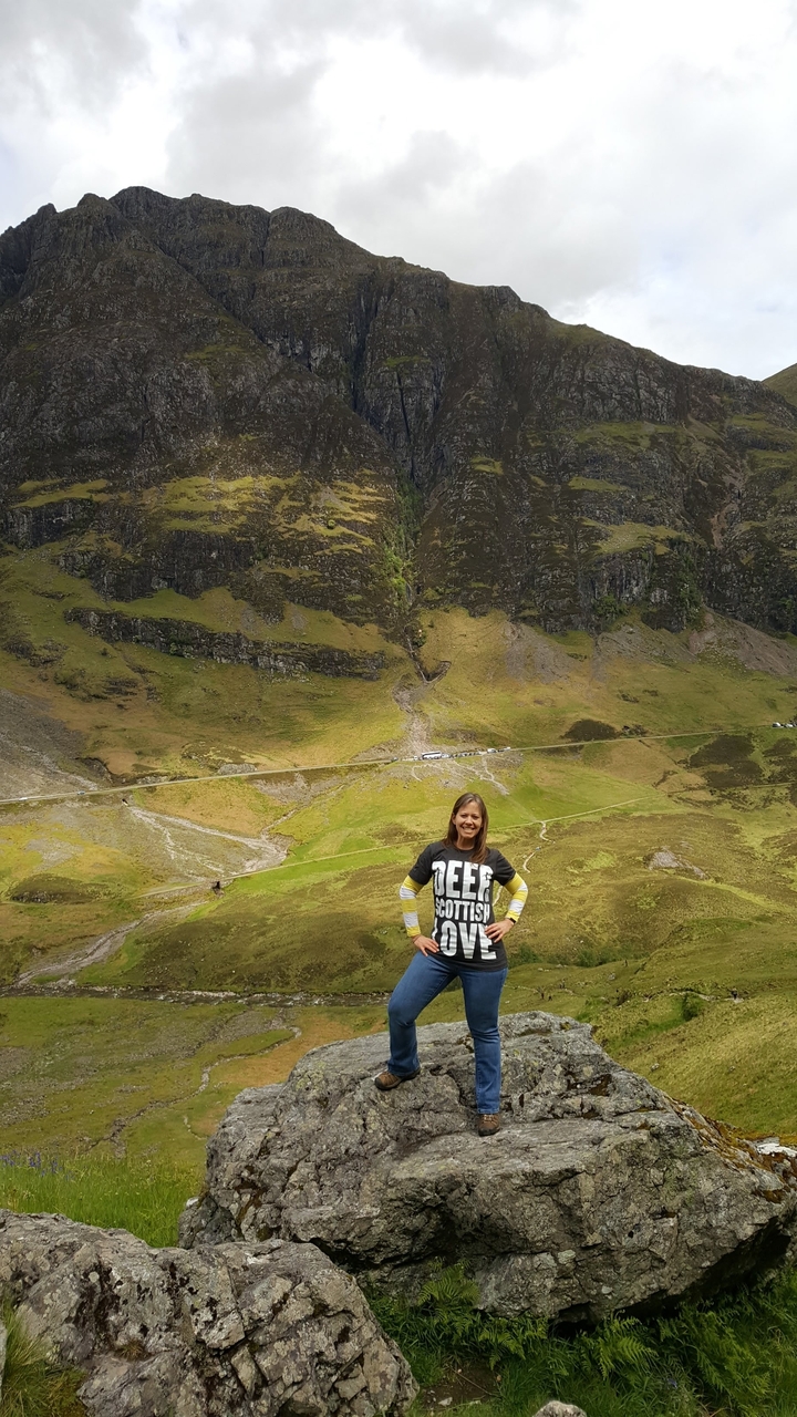 A person stands in front of the scenic hills wearing a 'Deep Scottish' shirt.