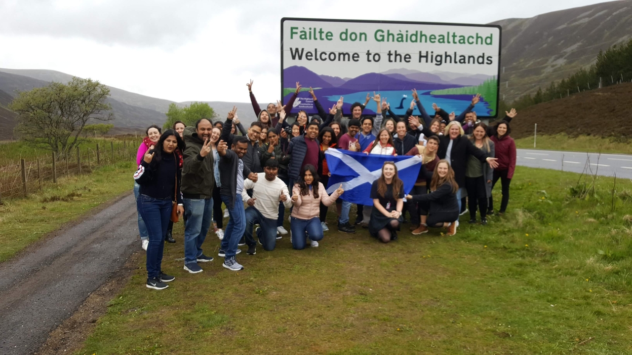 A group of people posing in front of a welcome sign to the Highlands.