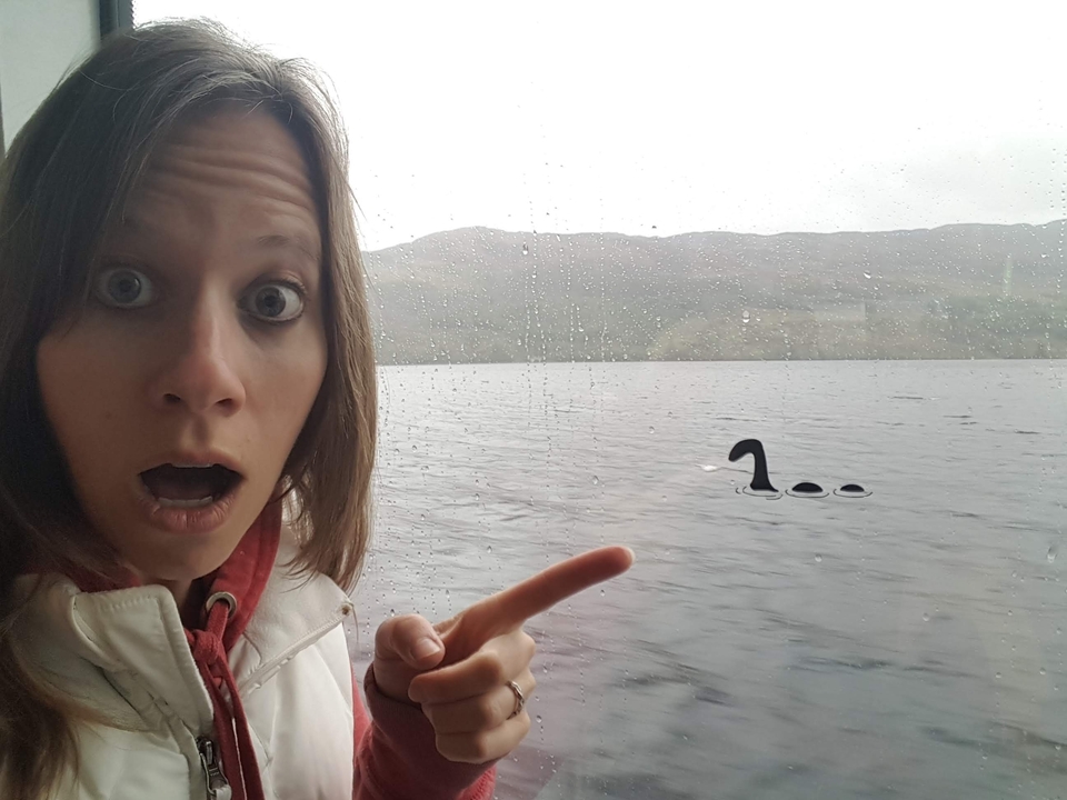 Une personne surprise pointant du doigt vers une fenêtre avec un faux monstre du Loch Ness dehors.