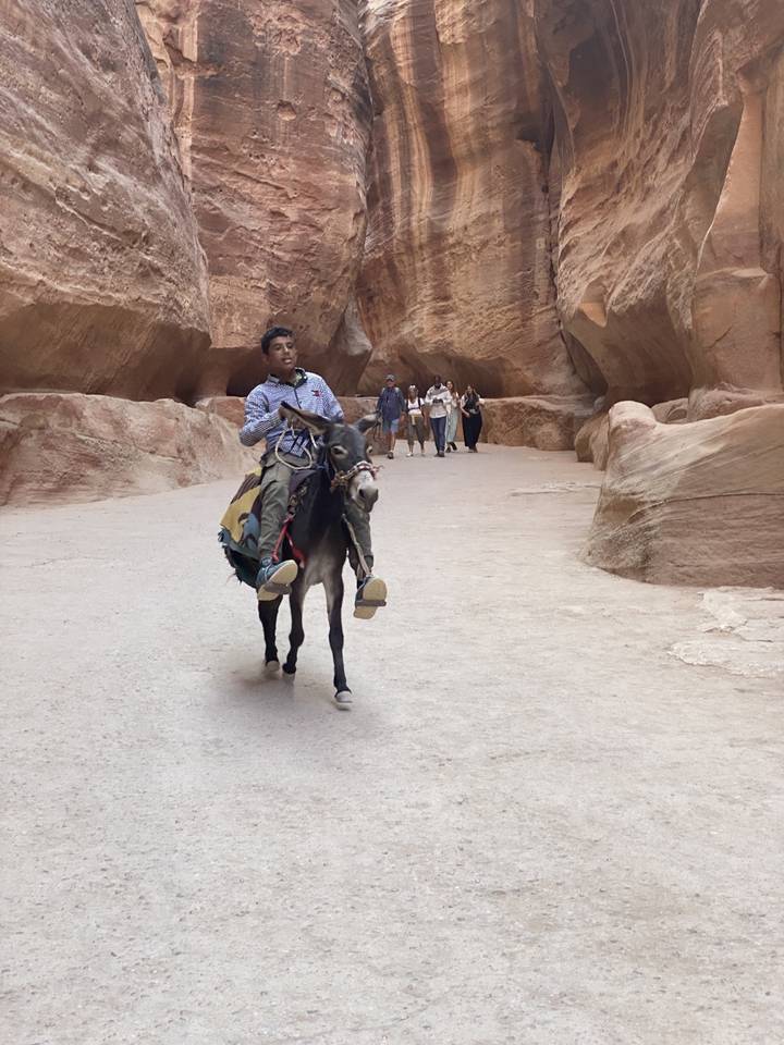 Person riding a donkey through a canyon with people in the background.
