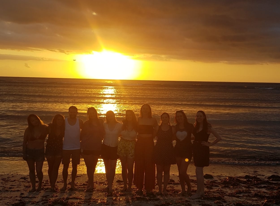 A group of people on a beach with a sunset over the ocean.
