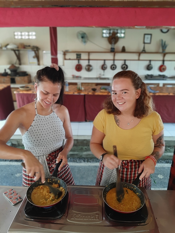 Two women smiling and cooking in an indoor setting.