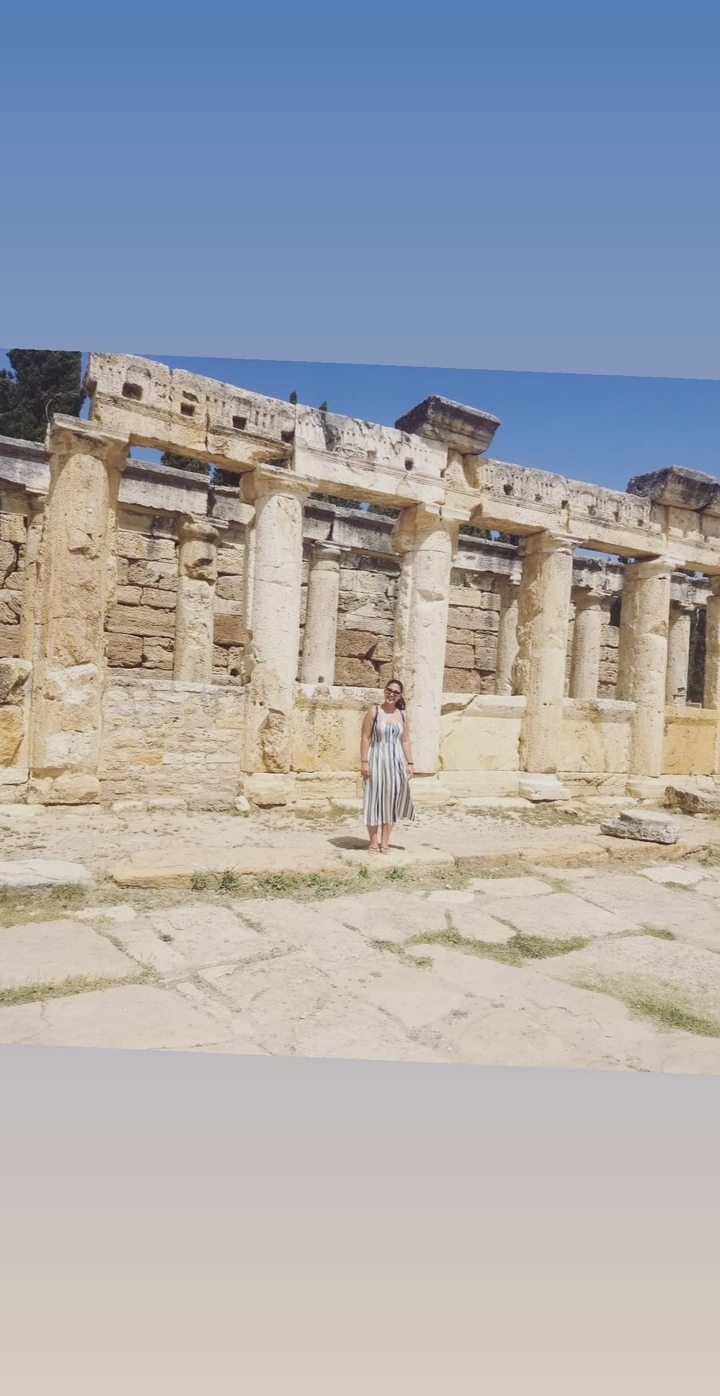 A person standing in front of ancient stone ruins with columns.