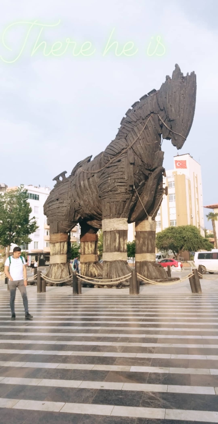 A large wooden horse statue resembling the Trojan Horse with people around.