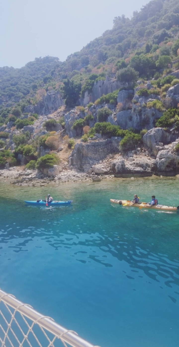 People kayaking in clear water near rocky shore.