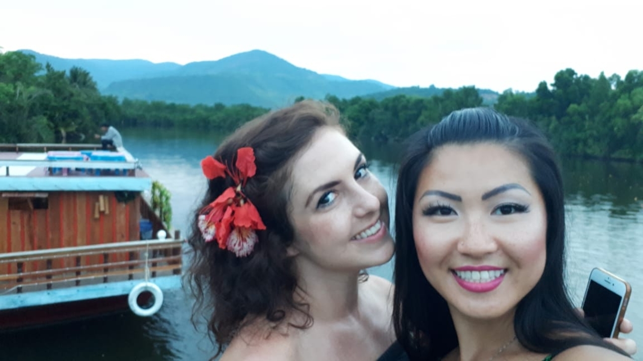 Two women smiling on a boat with water and hills in the background.
