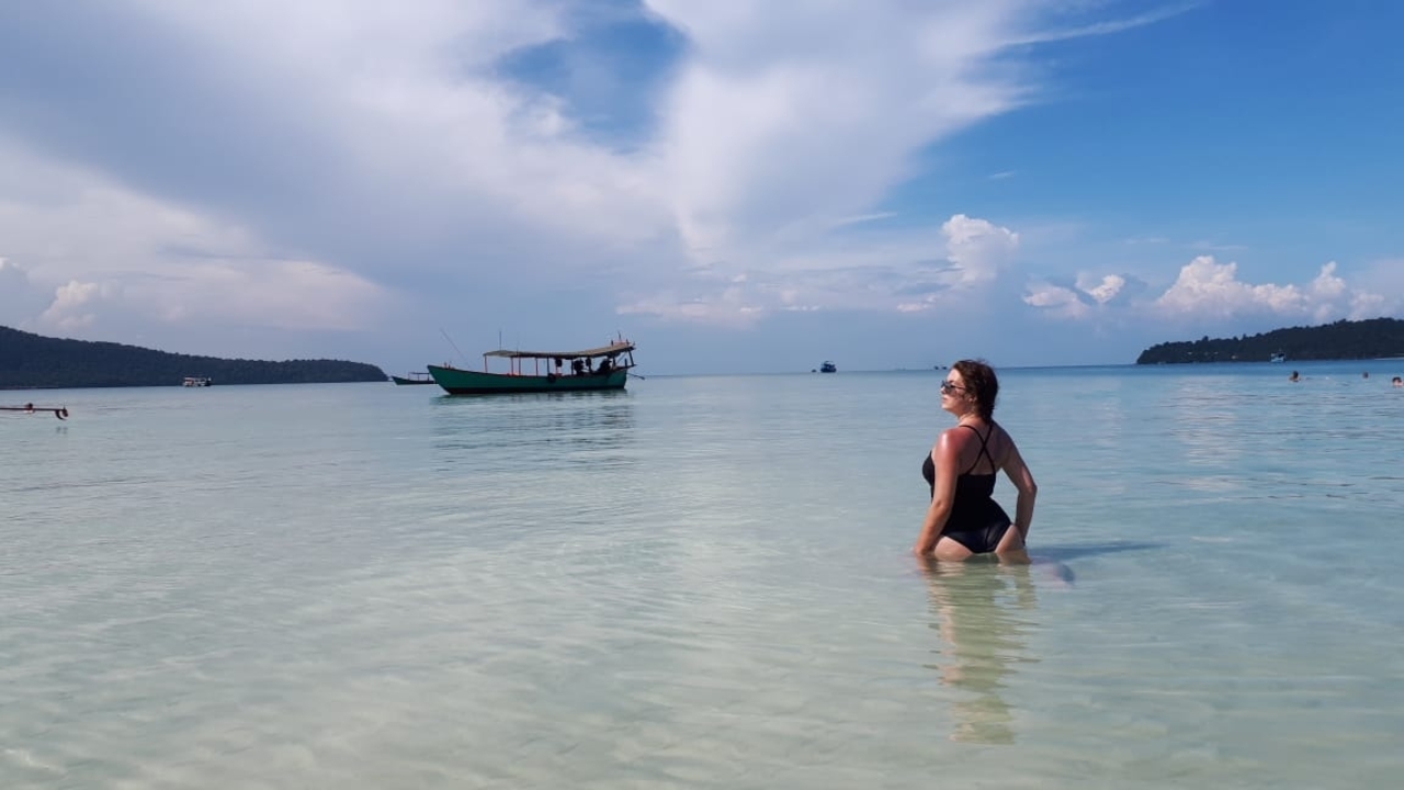 Woman wading in clear shallow water with a boat nearby.