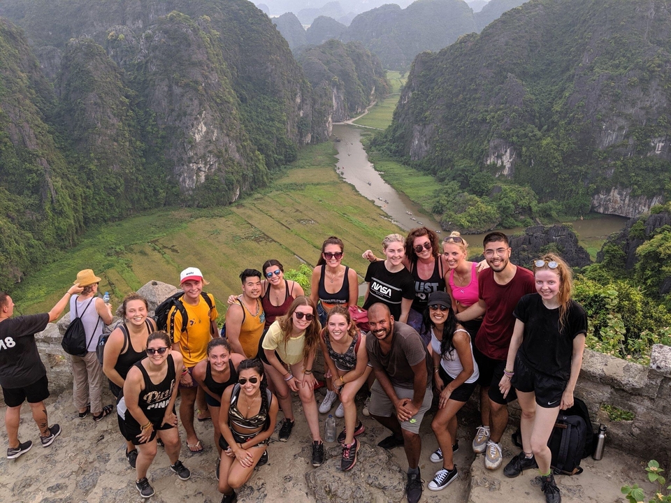 Group of people standing on a viewpoint overlooking a lush valley.