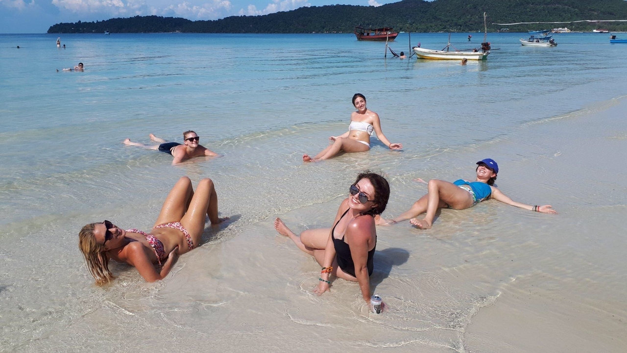 Women relaxing on a sandy beach with clear water.