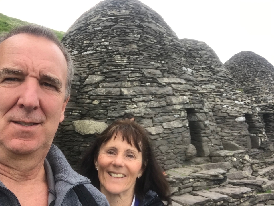 Two people smiling in front of stone beehive structures at Skellig Michael.
