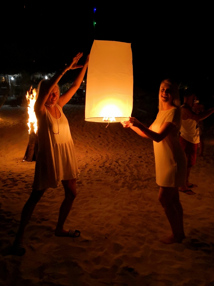 People launching a lantern on a beach at night.
