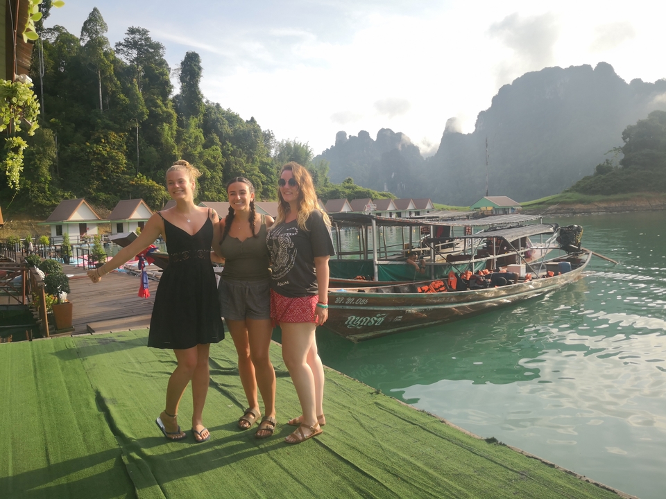 Group of people posing by a lake with boats and scenic cliffs.