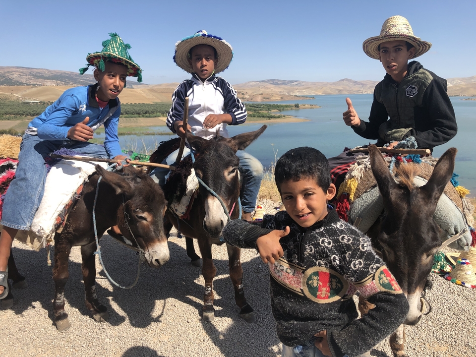 Children riding donkeys with a scenic background of a water body.