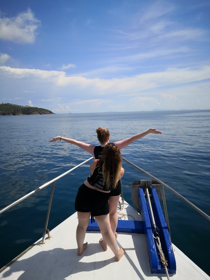 People posing on a boat, arms outstretched, with the ocean as the backdrop.