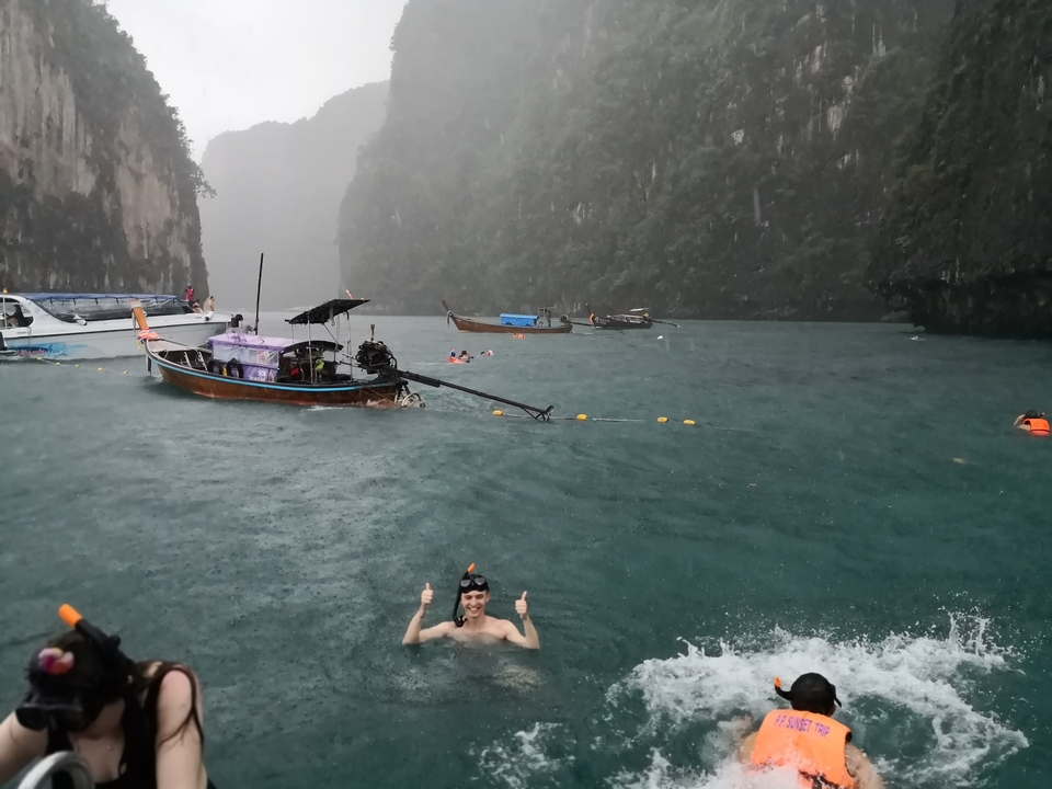 Person swimming in rain with boats around.