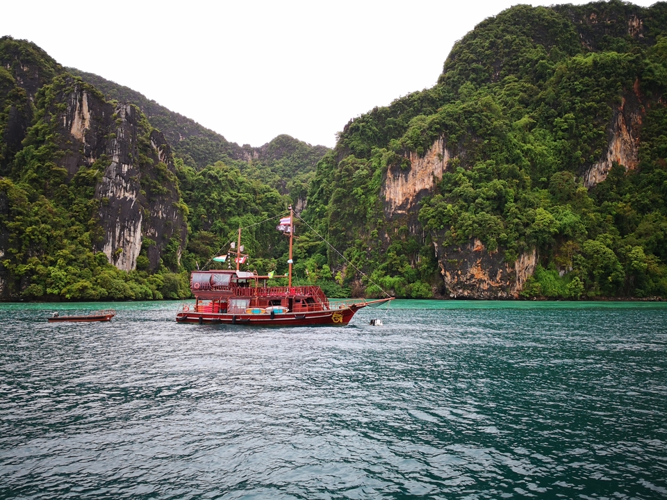 A traditional boat on blue waters with steep cliffs.